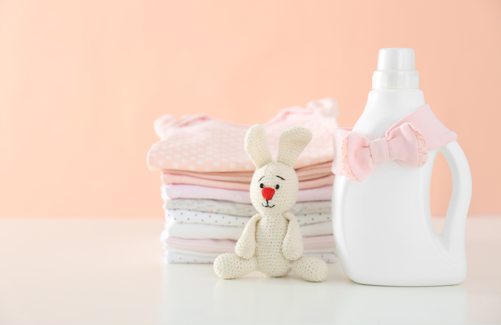 Detergent, toy and children's clothes on white table near pink wall